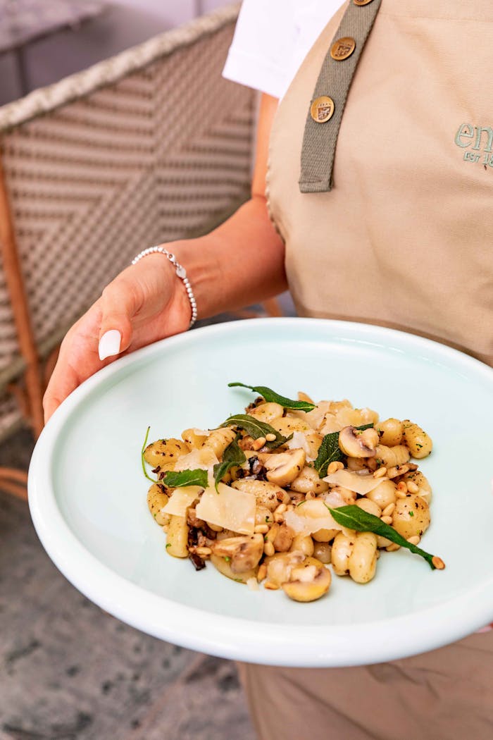 Close-up of a woman serving a delicious gnocchi dish with mushrooms and fresh herbs outdoors.